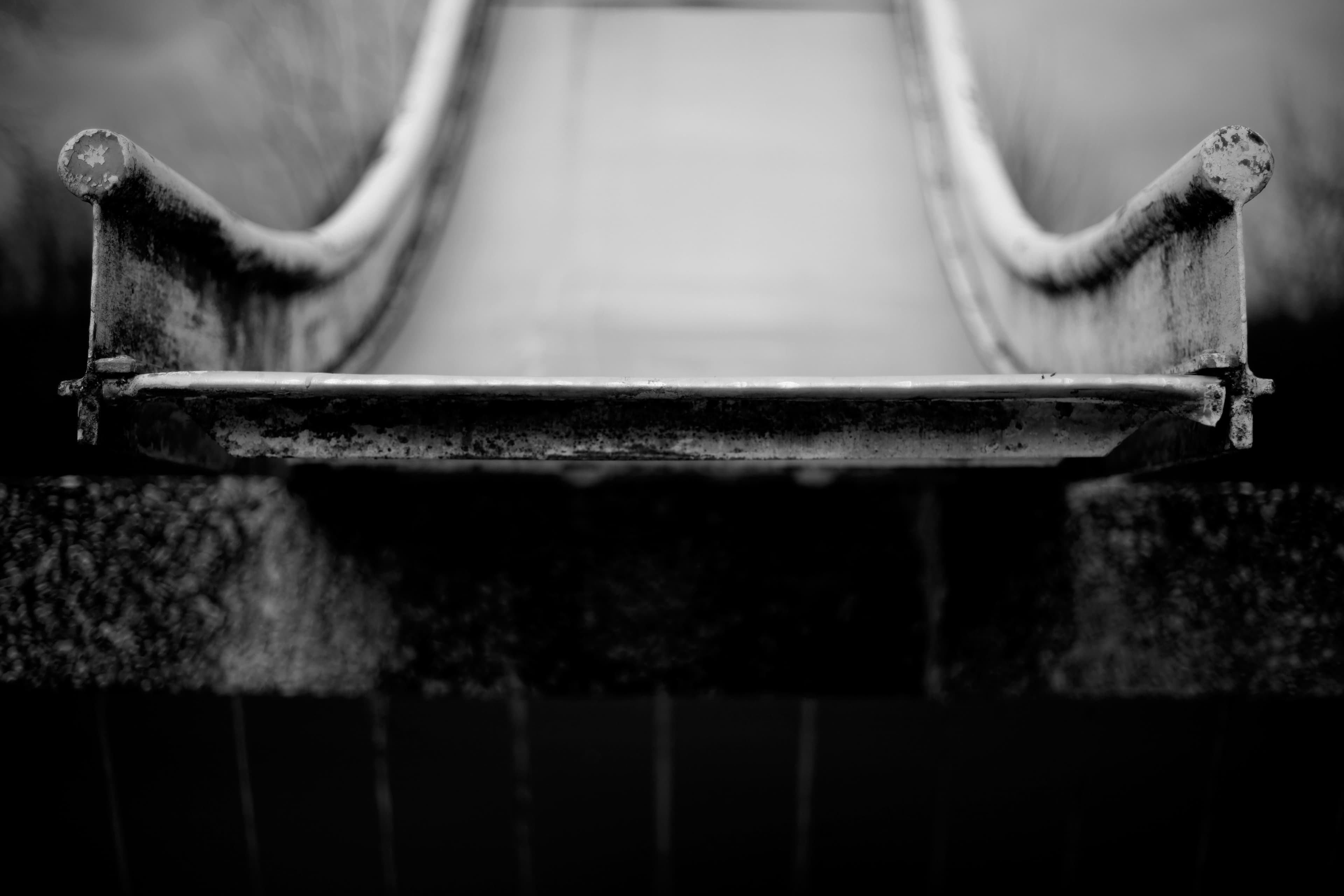 Close-up black and white photo of the bottom of a weathered metal playground slide.